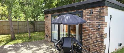 A patio with a table and chairs, a black umbrella, and a brick building with glass doors.
