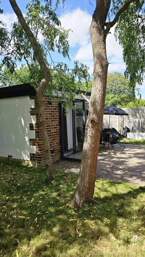 A backyard with a small brick building, a tree, and a patio area. - Quiet & Cosy Garden House Next to Beverley Park (London)