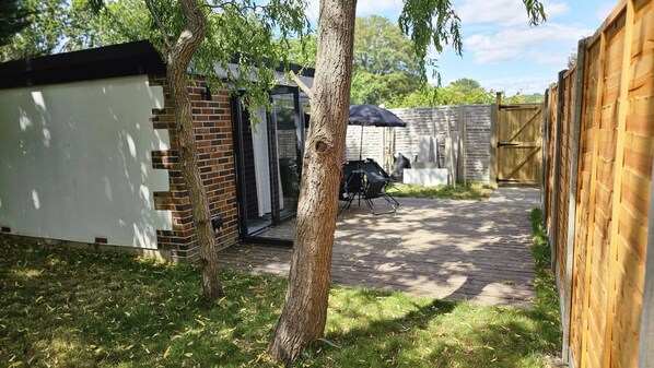 Un patio trasero con terraza de madera, pared de ladrillo y un cobertizo pequeño.