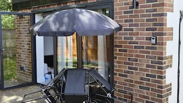 A modern outdoor seating area with a table and chairs, a large umbrella, and a brick wall.