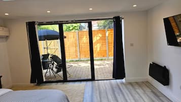 A bedroom with a sliding glass door to a patio, a bed, a desk with a chair, and a TV mounted on the wall.