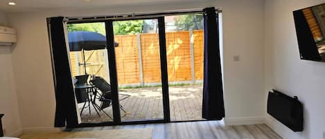 Un dormitorio con puerta corrediza de vidrio a un patio, una cama, un escritorio con silla y un televisor fijado a la pared.
