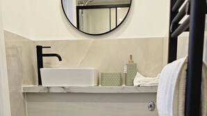 Et badeværelse med toilet, vask, spejl og et håndklædestativ.
