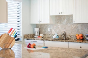 A kitchen with white cabinets, a granite countertop, a coffee maker, and a sink. - Your Fort Myers Beach Escape | Relax & Unwind (Fort Myers Beach)