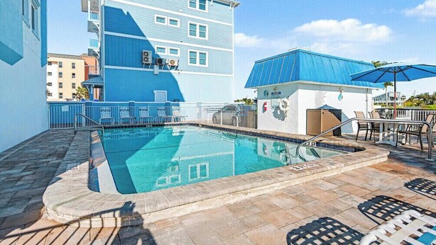 Une piscine dotée d’un parasol, de chaises longues et d’un bâtiment à la façade bleue.