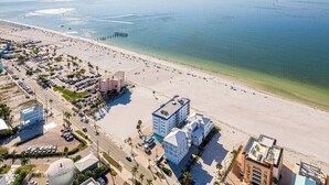 Vue aérienne d’une zone côtière avec une plage, une jetée et des bâtiments dotés de parkings.