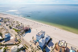An aerial view of a coastal area with a beach, a pier, and buildings with parking lots. - Your Fort Myers Beach Escape | Relax & Unwind (Fort Myers Beach)