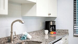 Una cucina con piano di lavoro in granito, lavello in acciaio inox, mobili bianchi e una macchina per il caffè.