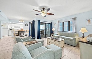 Ein geräumiges Wohnzimmer mit Deckenventilator, ein Essbereich mit Tisch und Stühlen sowie eine Küche im Hintergrund.