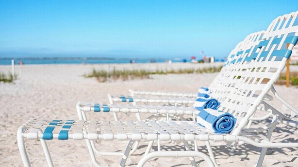Una spiaggia con sedie a sdraio bianche e asciugamani blu.