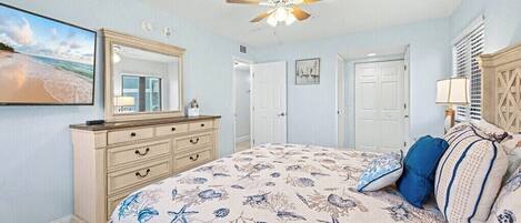 A bedroom with a bed, dresser, ceiling fan, and a large window.