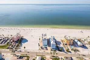 Eine Luftaufnahme eines Hotels direkt am Strand, mit mehreren Gebäuden, einem Parkplatz und freiem Blick auf den Ozean.