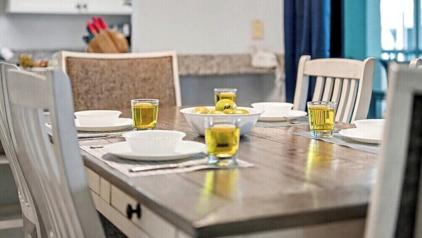 A dining table set with plates, bowls, and glasses of a yellow beverage, likely tea, in a modern kitchen with white cabinets and a blue curtain in the background. - Private 2BR Stay | Your Fort Myers Beach Getaway (Fort Myers Beach)