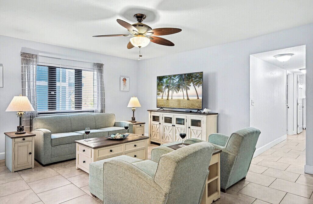 Ein Wohnzimmer mit Sofa, Sesseln, Couchtisch, Fernseher und Deckenventilator.