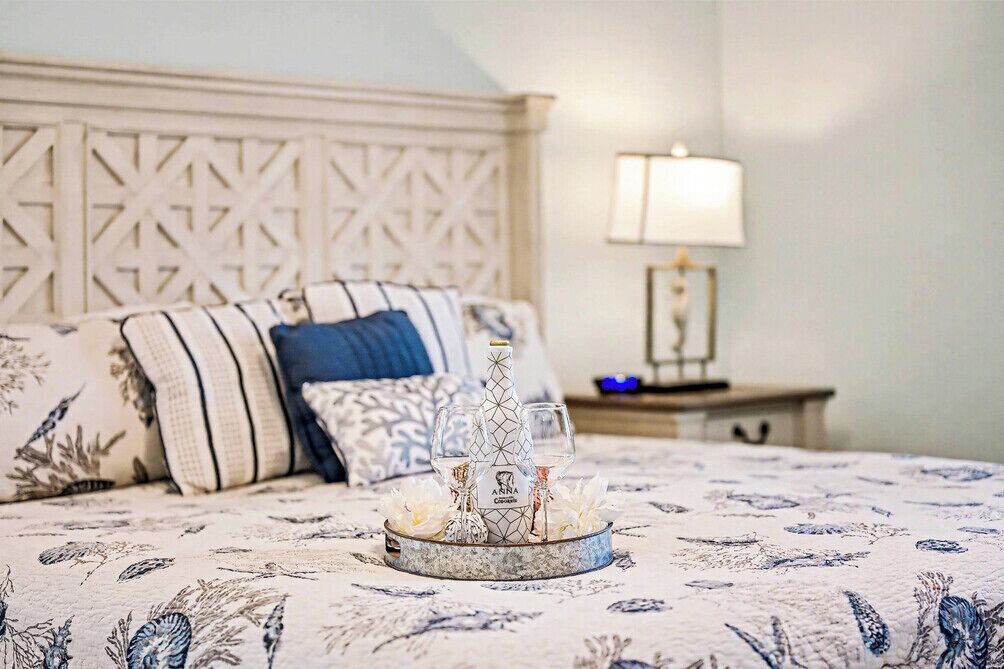 A bed with a floral-patterned bedspread, a decorative tray with glasses and a bottle, and a nightstand with a lamp.