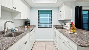 A modern kitchen with white cabinets, granite countertops, a built-in oven, and a window with blinds. - Poolside 2BR Condo with Balcony near Beach Pier (Fort Myers Beach)