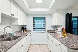 Eine moderne Küche mit weißen Schränken, Granit-Arbeitsplatten, einem eingebauten Ofen und einem Fenster mit Jalousien.