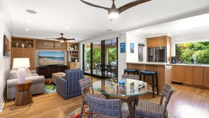 A modern living room with a glass-top dining table, wicker chairs, a sofa, a TV, and ceiling fans. - Wailea Ekahi 42C - Peekaboo Ocean Views, 2 Full Baths, King Tempurpedic, Full AC (Kihei)