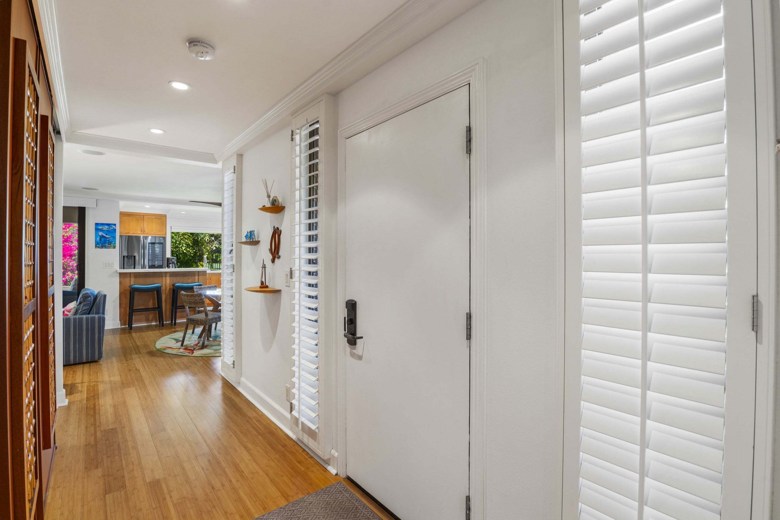 A hallway with a wooden floor, a white door, and a window with blinds.
