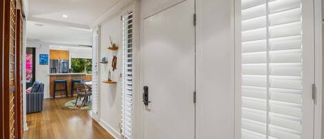 A hallway with a wooden floor, a white door, and a window with blinds.