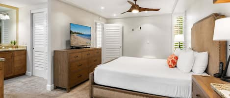 Une chambre à coucher comprenant un lit, une commode, un téléviseur, un ventilateur de plafond et une fenêtre avec des stores.