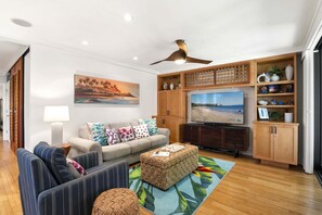 Una sala de estar con un sofá, un televisor y un ventilador de techo.