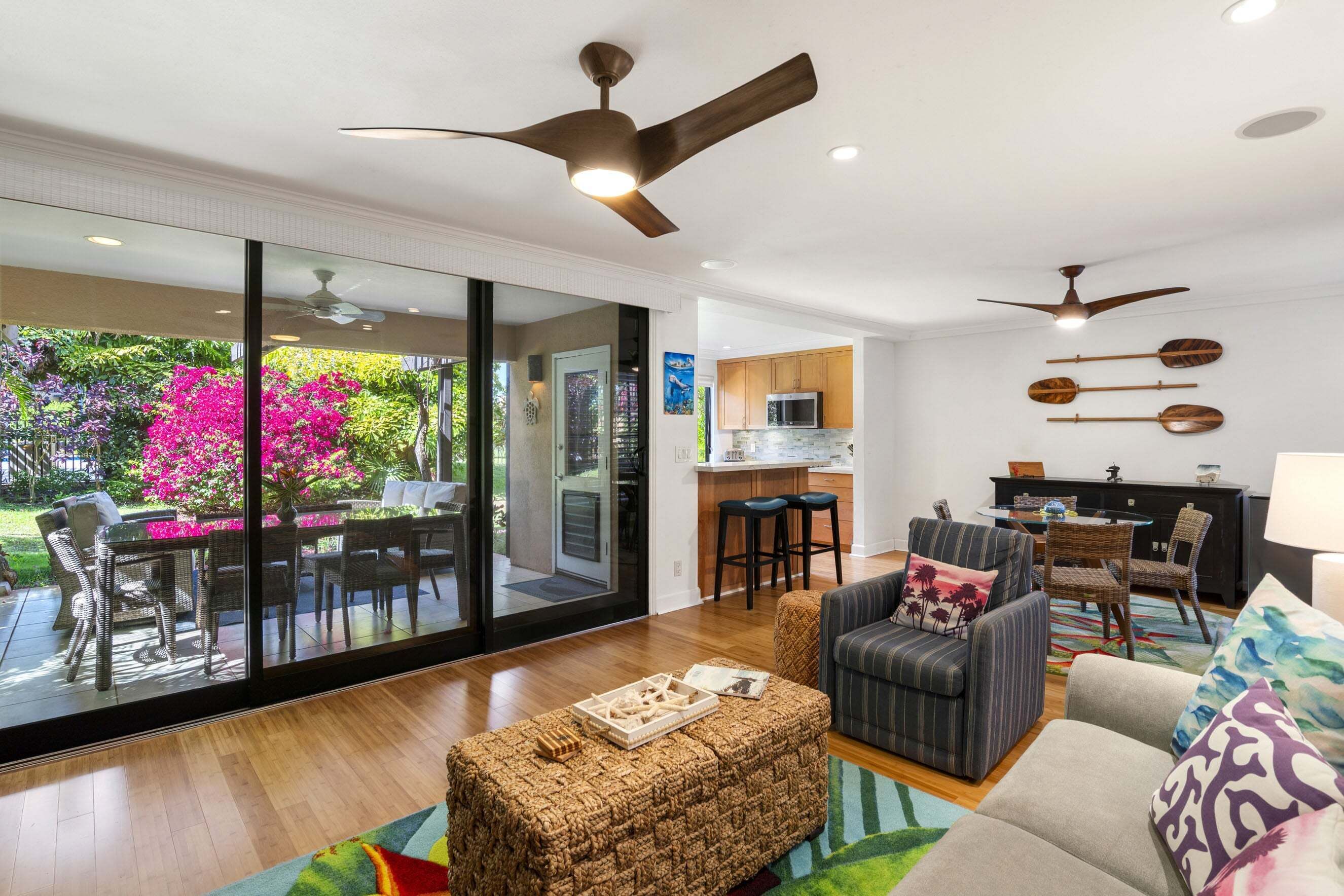 Un salon moderne doté d’une grande porte vitrée donnant sur un patio, d’un coin cuisine et d’un espace repas agrémenté d’un ventilateur de plafond.