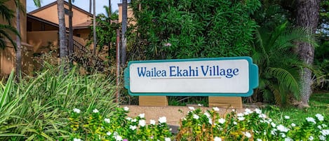 Letrero de Wailea Ekahi Village con exuberante follaje y un edificio de fondo.