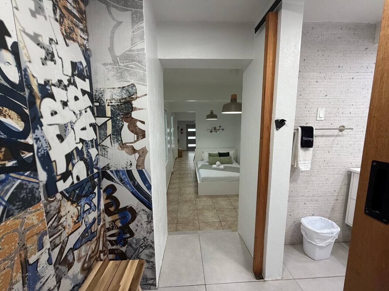 A hallway with a bed, a trash bin, and a wall with graffiti.