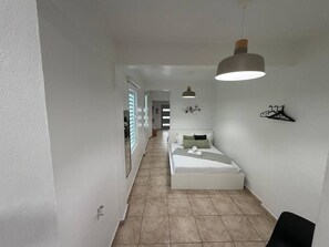 A narrow hallway leading to a bedroom with a bed, a hanging light fixture, and a wall-mounted coat rack. - Modern Santurce Apartment Near Beaches for 4 (San Juan de Puerto Rico)