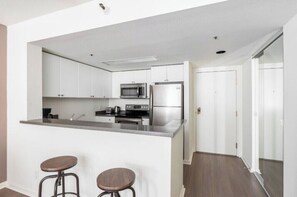 A compact kitchen with a microwave, stove, and refrigerator. There are two stools at the counter. - Charming 1BR Escape at South Beach Marina (San Francisco)