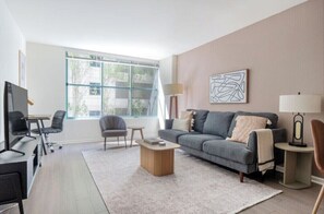 A modern living room with a grey sofa, a coffee table, and a TV on a stand. - Charming 1BR Escape at South Beach Marina (San Francisco)