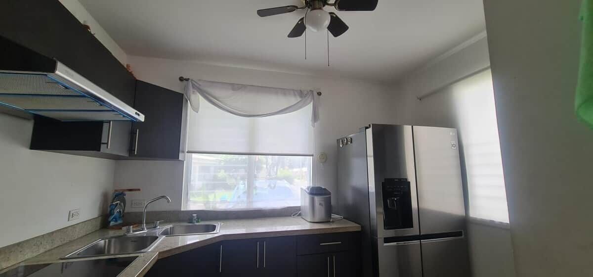 A compact kitchen with a built-in refrigerator, a window with a curtain, and a ceiling fan.