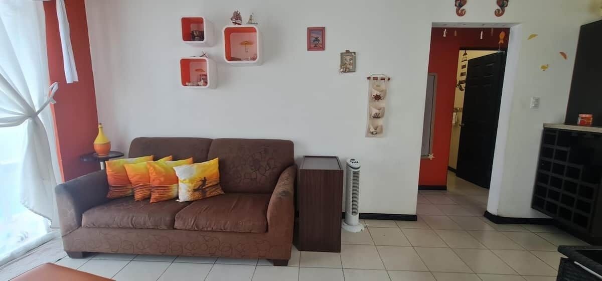 Uma sala de estar com um sofá marrom, um aquecedor e uma porta com moldura vermelha que dá para outro cômodo.