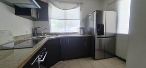 Une cuisine moderne dotée d’un réfrigérateur en acier inoxydable, d’un four encastré et d’une fenêtre avec un rideau.