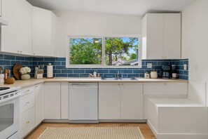A modern kitchen with white cabinets, a dishwasher, a sink, and a window with a view of trees.