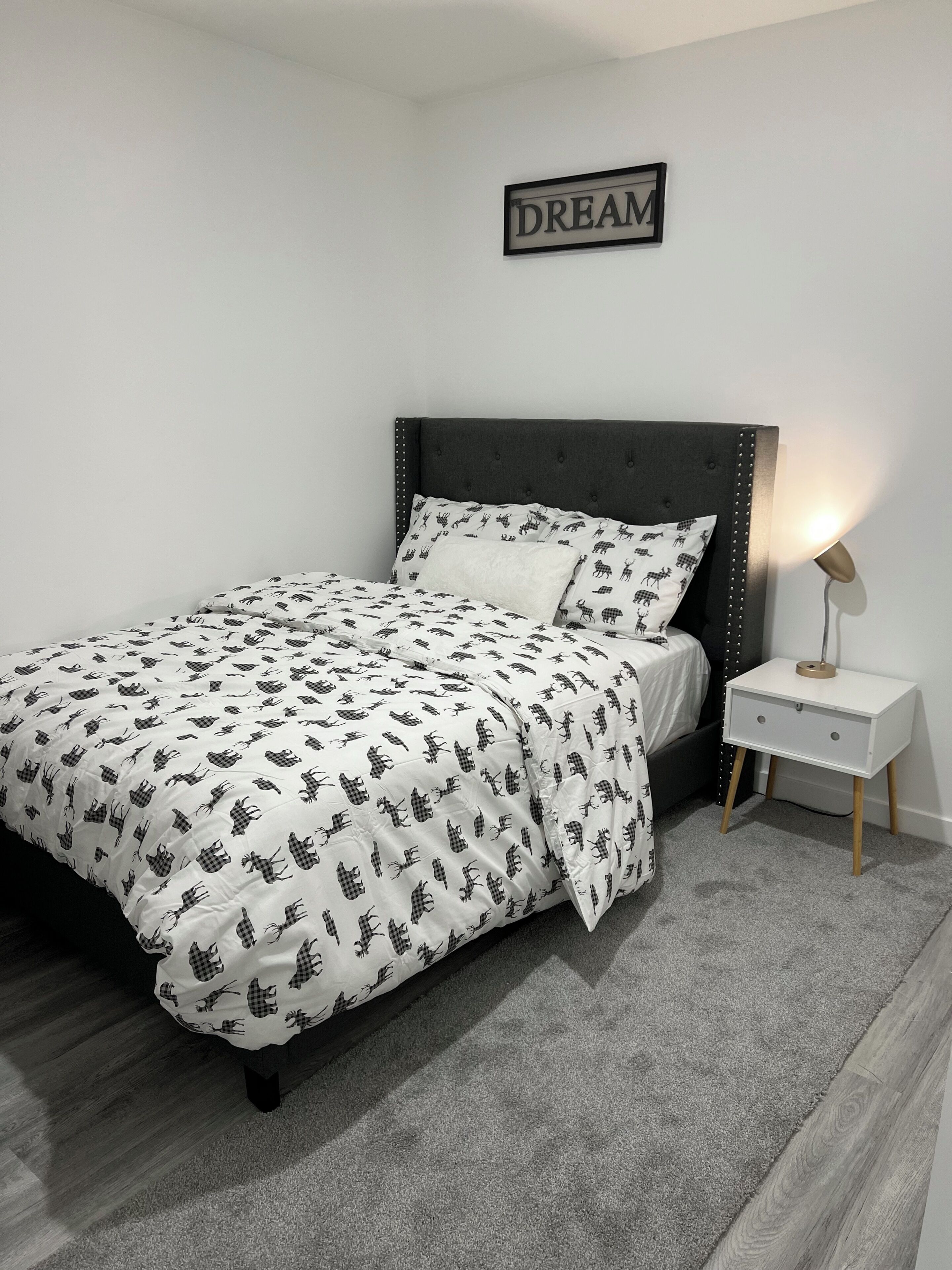 Una cama bien hecha con una colcha estampada, una lámpara de noche y un cartel en la pared que dice 'DREAM'.