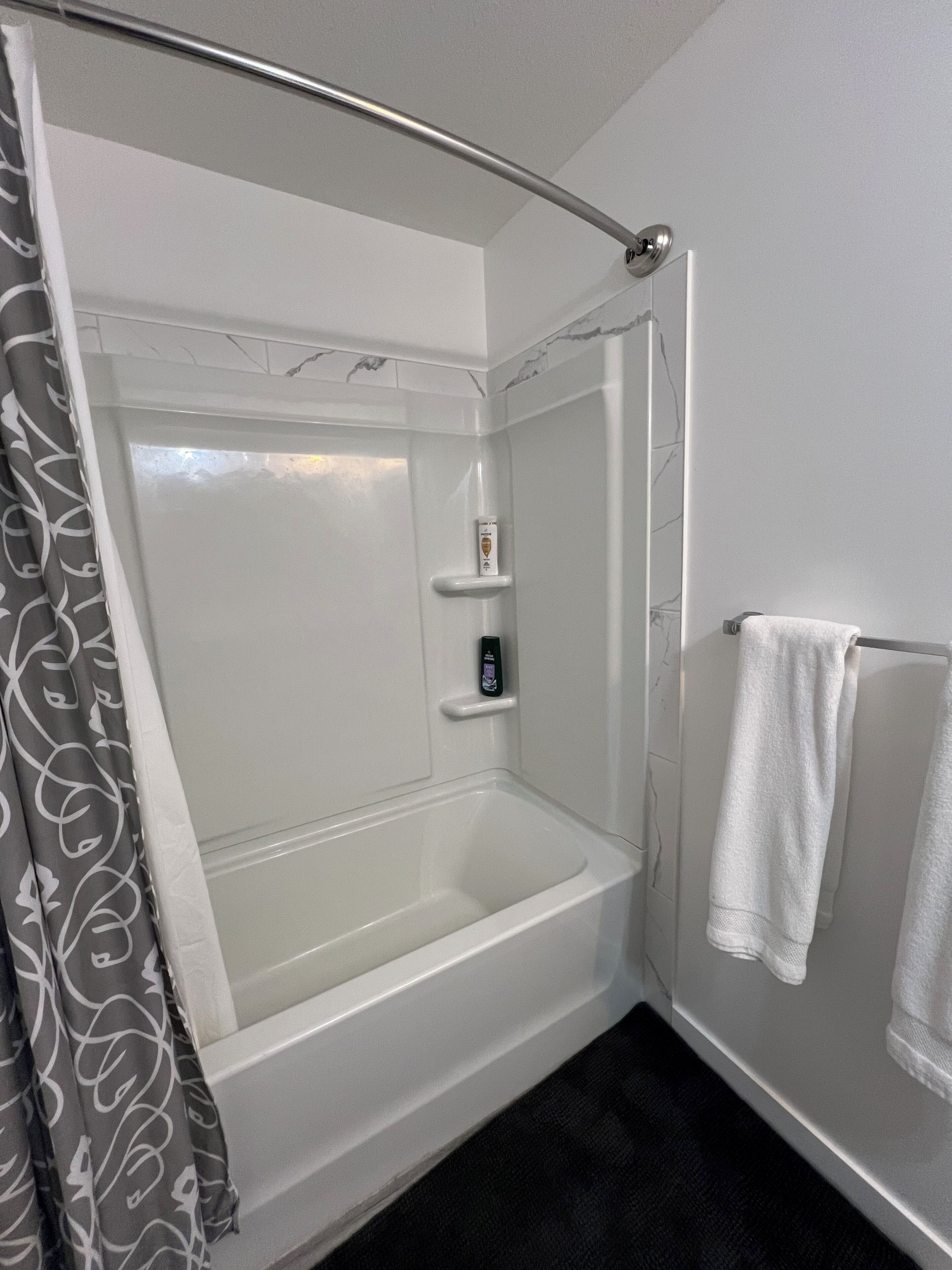A shower with a glass door, a white bathtub, a towel rack, and a shower control panel.