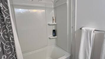 A shower with a glass door, a white bathtub, a towel rack, and a shower control panel.