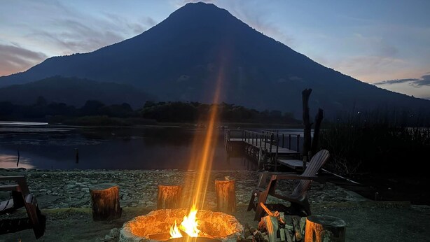 A campfire with logs around it, a wooden deck, and a mountain in the background. - Beautiful private villa with lovely gardens and trees (Santiago Atitlán)