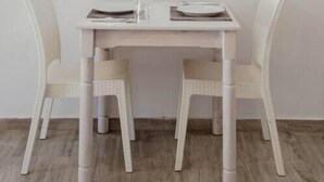 A white dining table with two chairs, a single light fixture above, and a small table with a cup and saucer. - White Wave Studios (santorini)