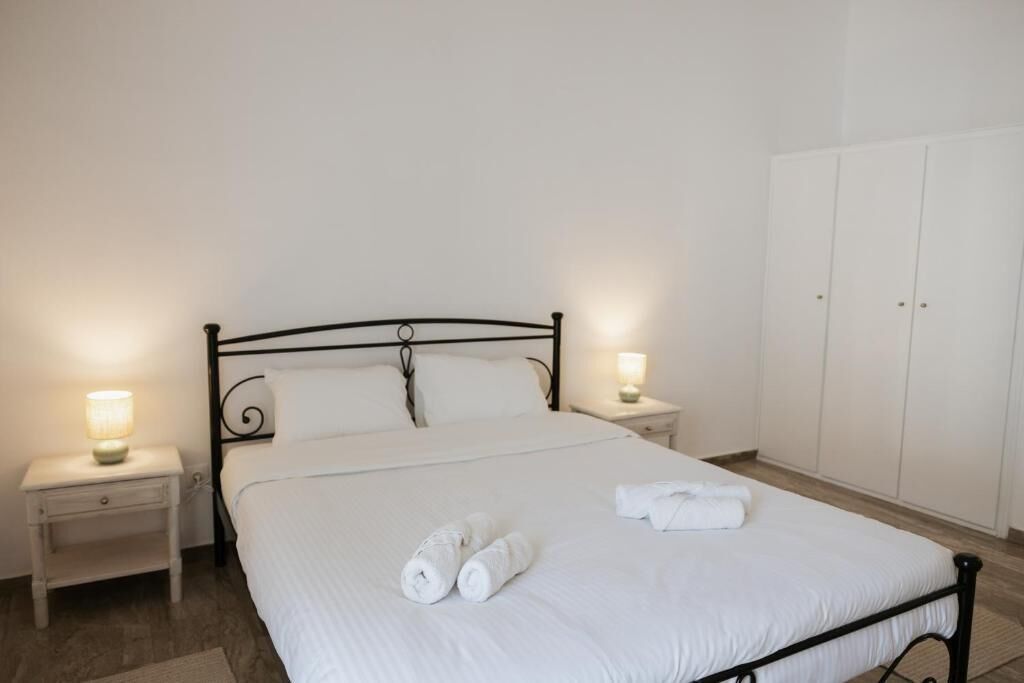 A neatly made bed with white linens and rolled towels, two bedside tables with lamps, and a wardrobe in a simple, clean room.