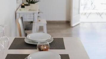 Un coin repas avec une table dressée pour deux personnes, un téléviseur fixé au mur et une vue sur l’extérieur.