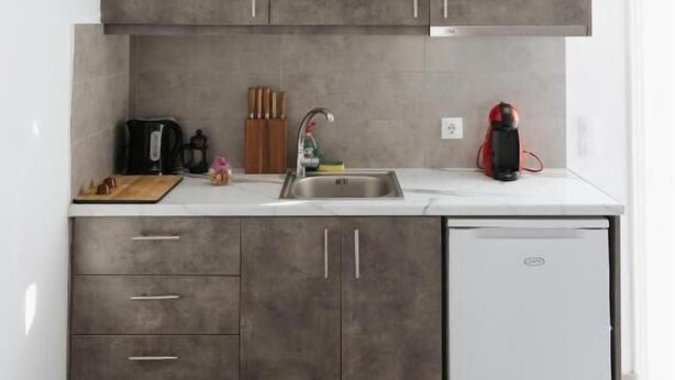 A compact kitchen with grey cabinets, a white countertop, a built-in oven, and a small refrigerator. - White Wave Studios (santorini)