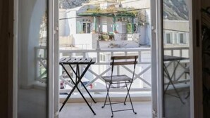 An open door leading to a balcony with a table and chair, overlooking a mountainous landscape. - White Wave Studios (santorini)