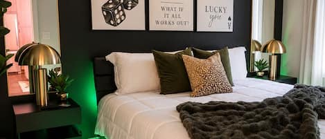 A modern bedroom with a bed, green ambient lighting, a ceiling fan, and wall art.