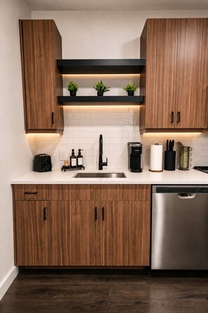 A modern kitchen with wooden cabinets, a stainless steel dishwasher, and a black countertop. - Stylish West Midtown Retreat - Pool & Balcony (Atlanta)