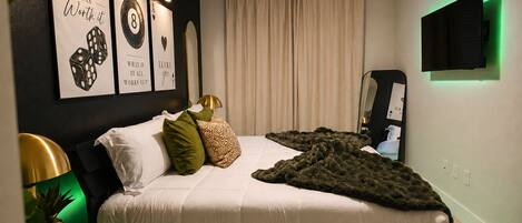 A bedroom with a bed, pillows, a blanket, a wall-mounted TV, and framed motivational posters.