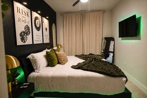 Ein Schlafzimmer mit einem Bett, Kissen, einer Decke, einem an der Wand montierten Fernseher und gerahmten Motivationspostern.