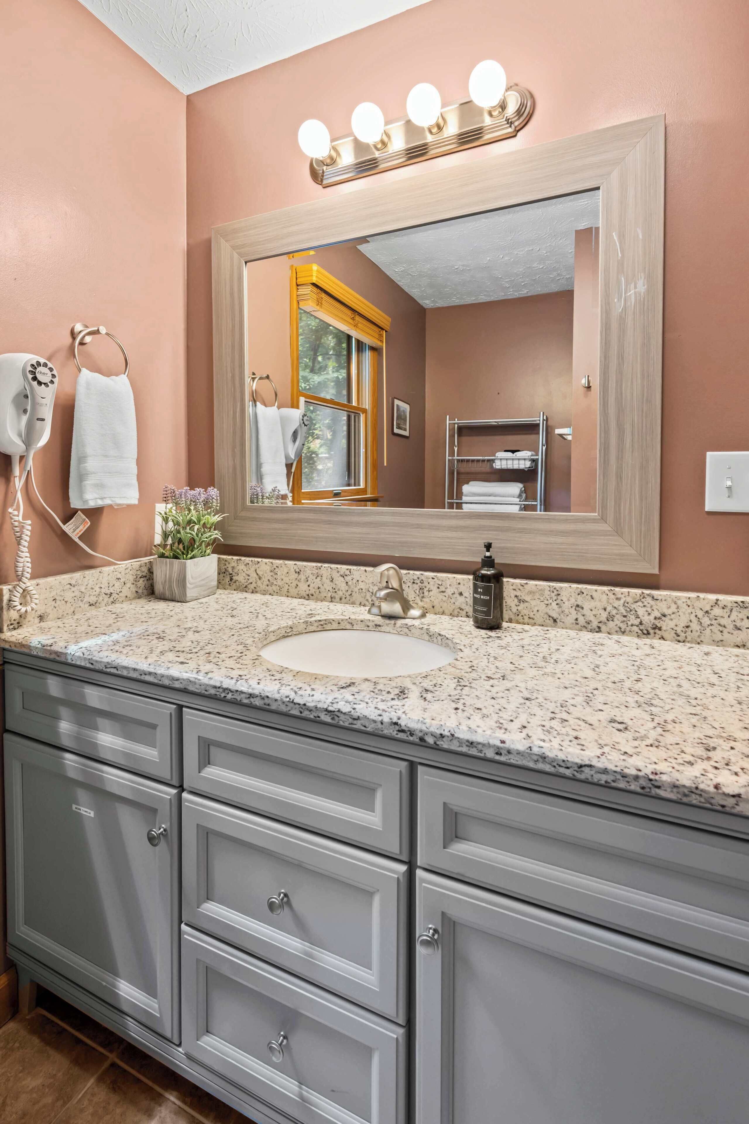 A bathroom with a granite countertop, a sink, a mirror with lights, a towel rack, and a vanity with drawers.